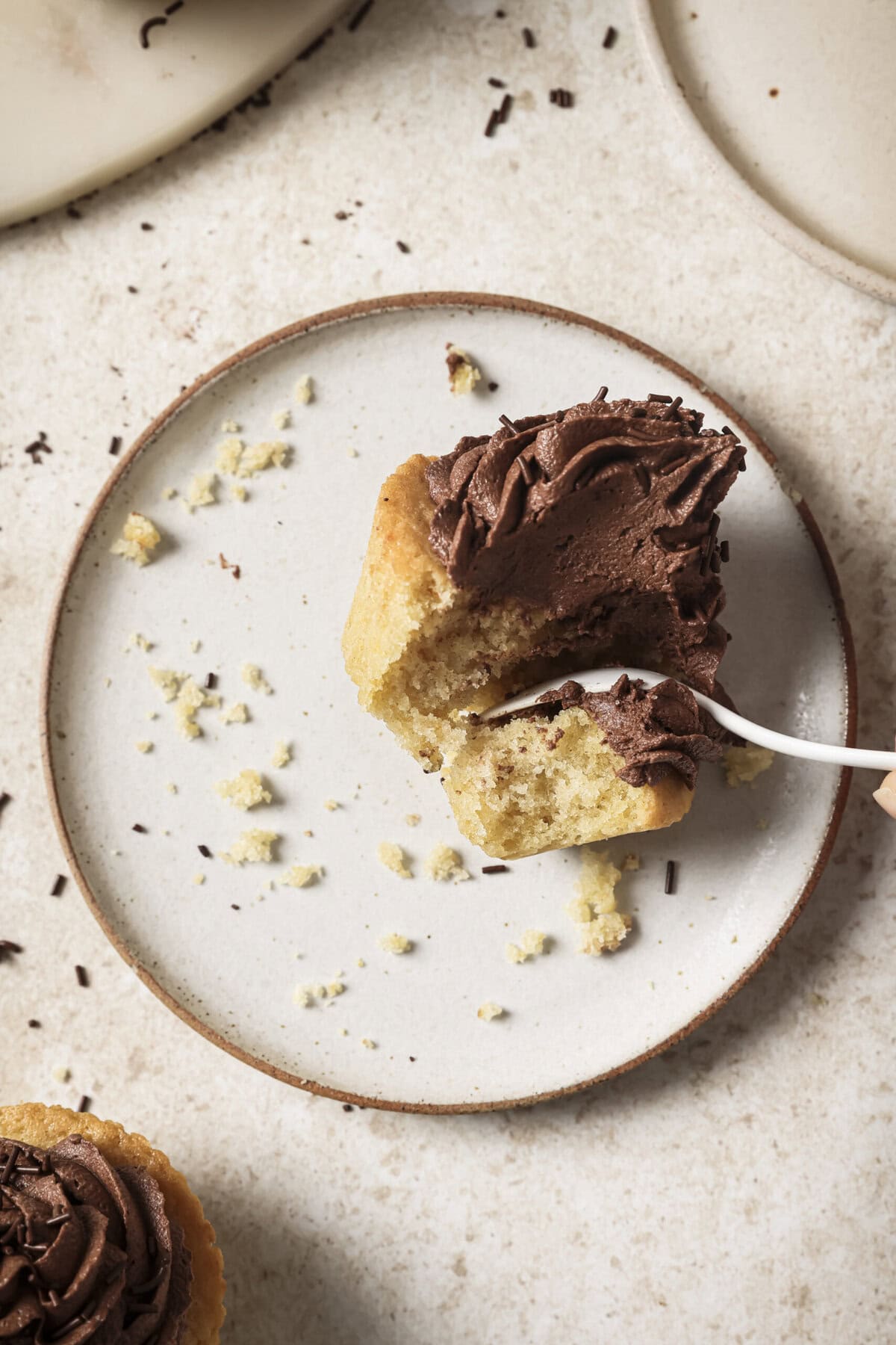 Overhead view of person digging into a cupcake on a plate with a spoon.