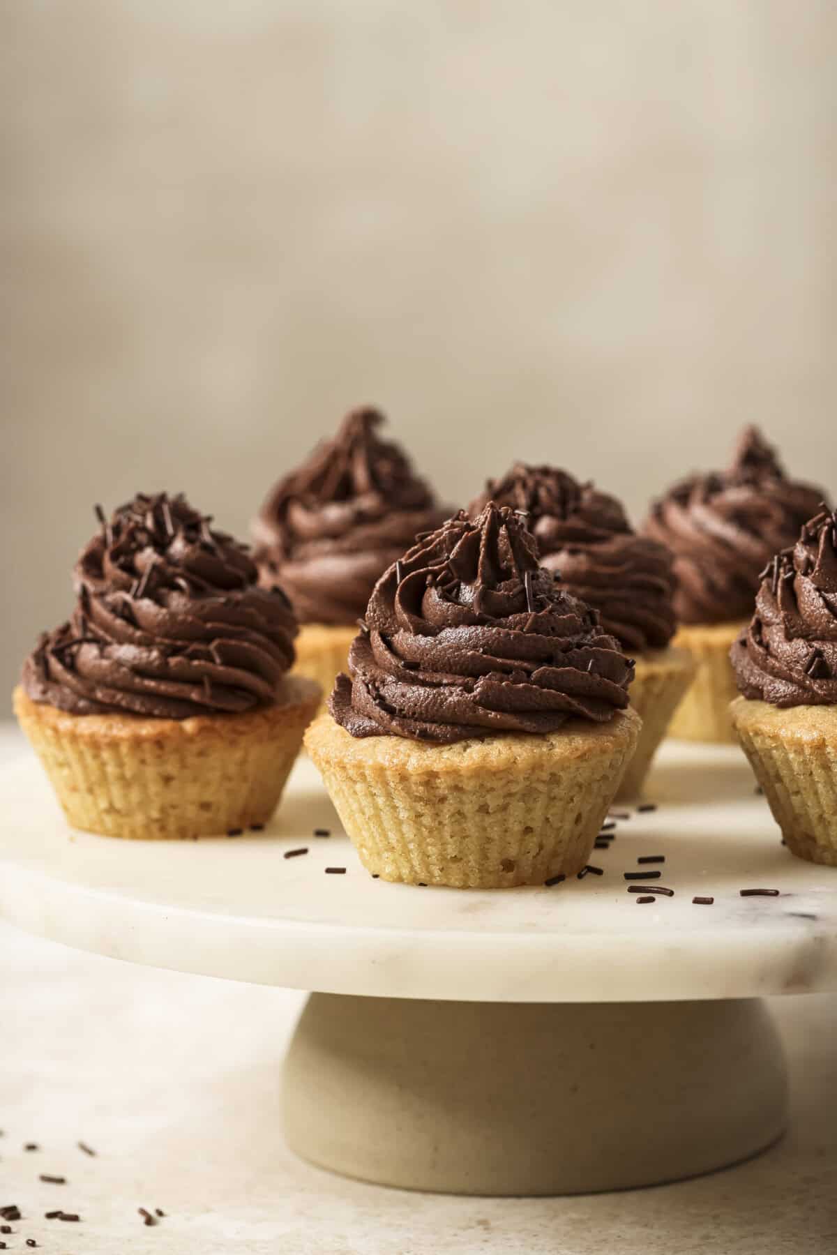 Close up side view of 6 chocolate frosted cupcakes on a raised marble serving tray.