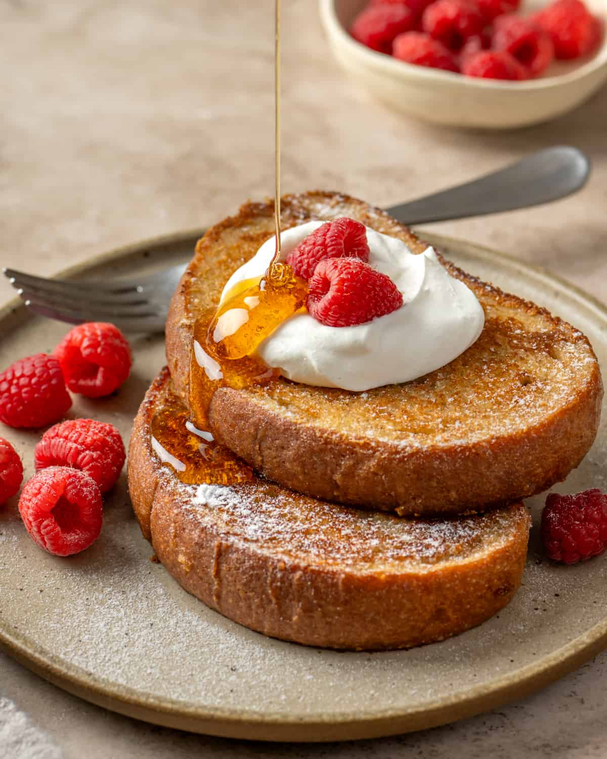 Side view of someone pouring maple syrup on two slices of vegan french toast.