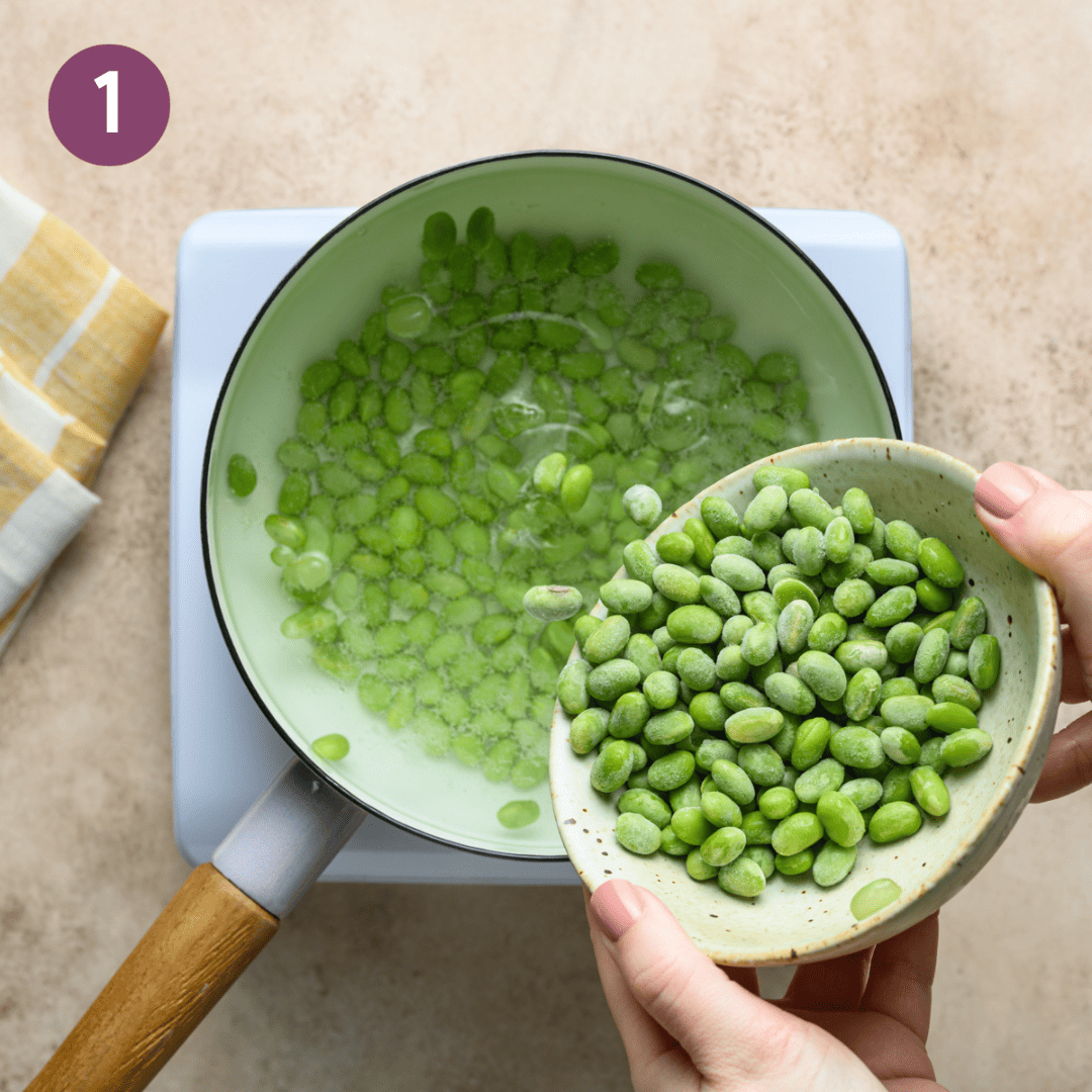 Person adding frozen edamame to a pot of hot water.