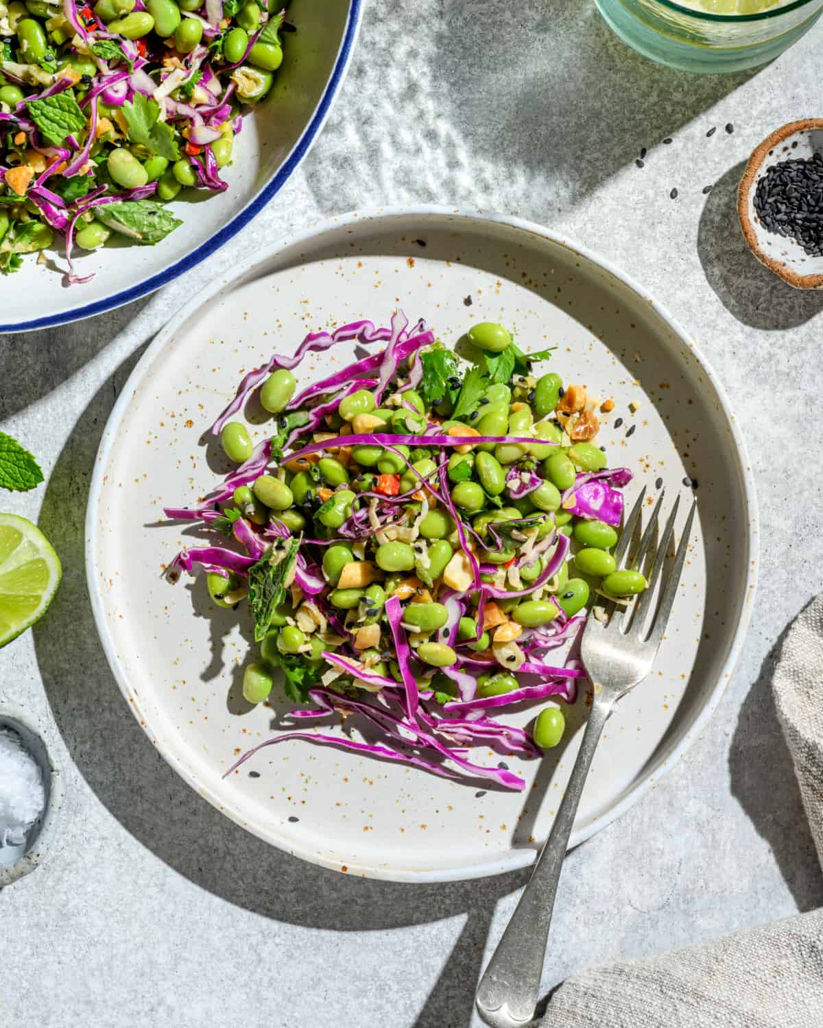 Two plates of edamame salad on a white table.