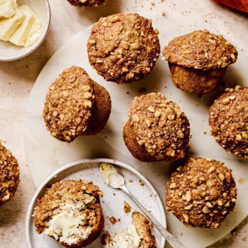 Baked banana muffins on a serving platter with one muffin sliced open and buttered.