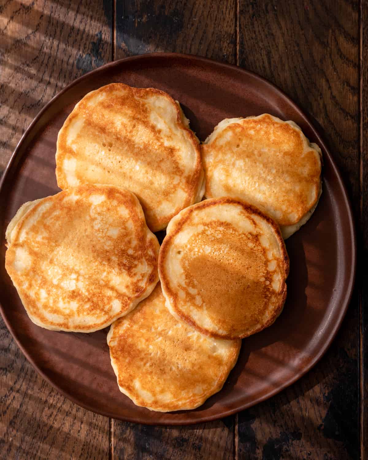 crispy edged vegan pancakes spread out on a brown plate in morning sunlight.