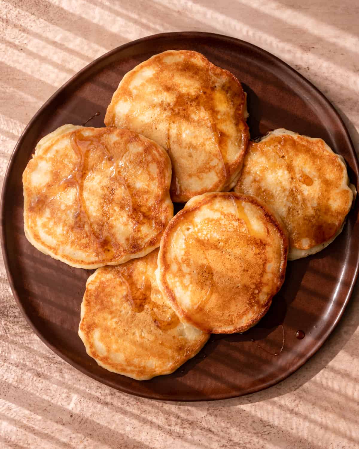 crispy edged vegan pancakes spread out on a brown plate in morning sunlight.