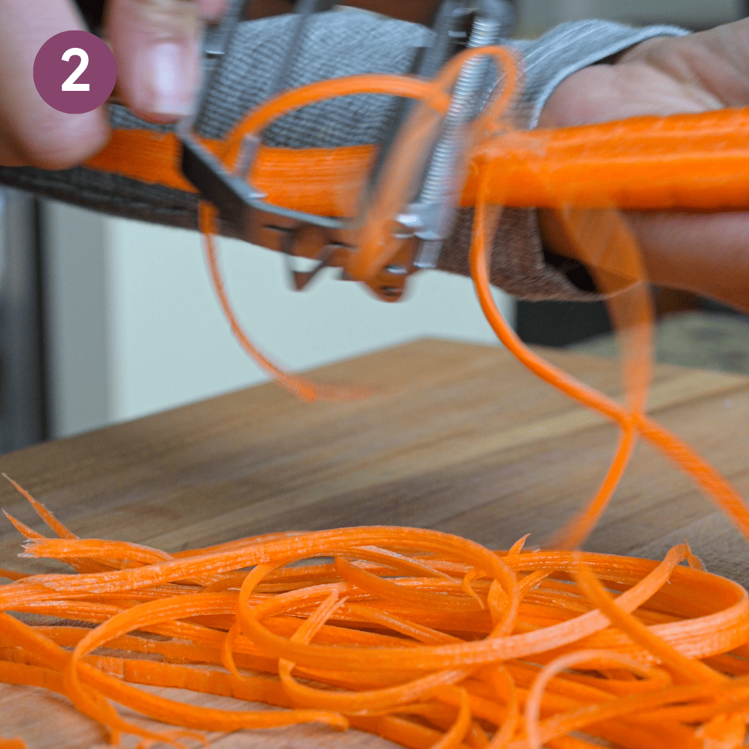 person shredding carrots onto a cutting board.