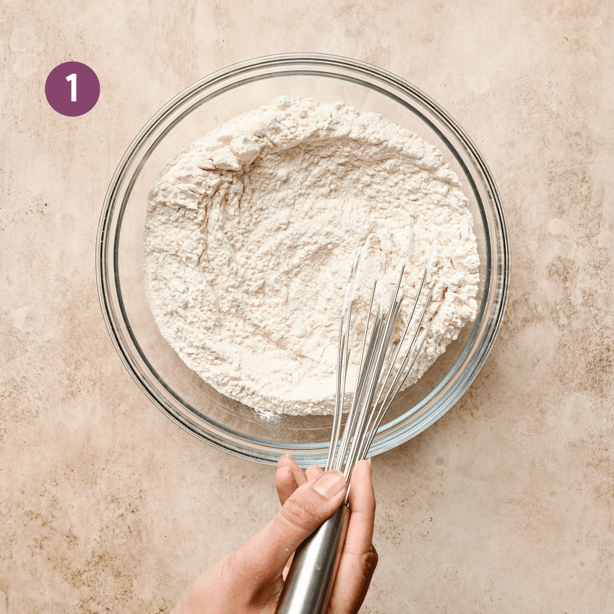 woman's hands whisking dry ingredients in a glass bowl for vegan lemon cake.