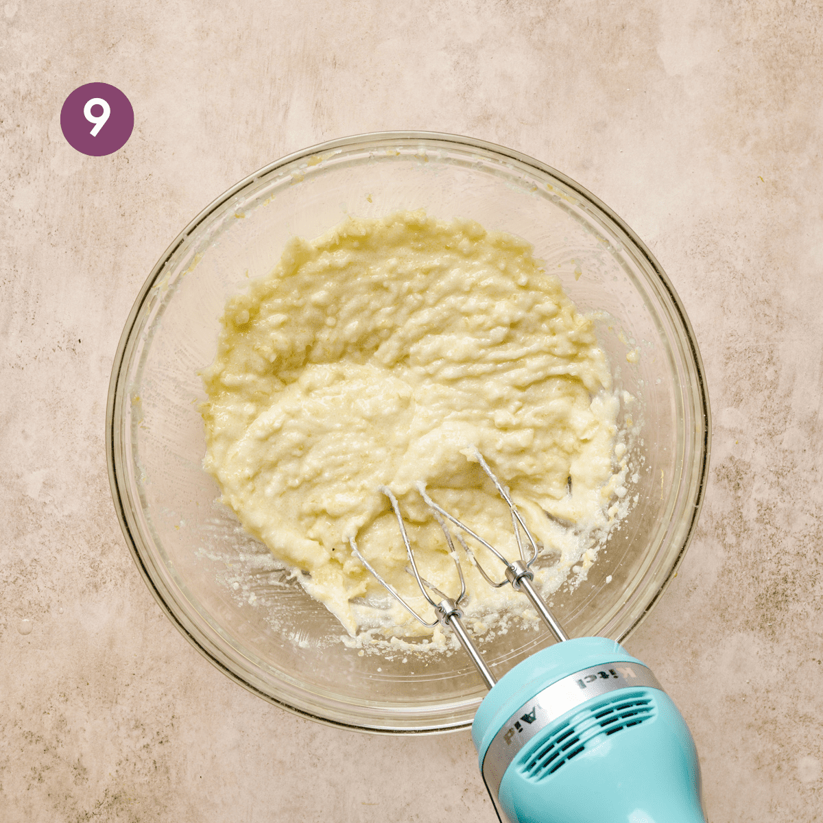 light blue electric mixer whipping vegan butter and oil with sugar until fluffy in a glass bowl.