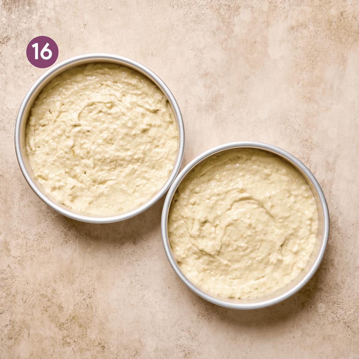 vegan lemon cake batter in two round cake pans on a light pink surface.