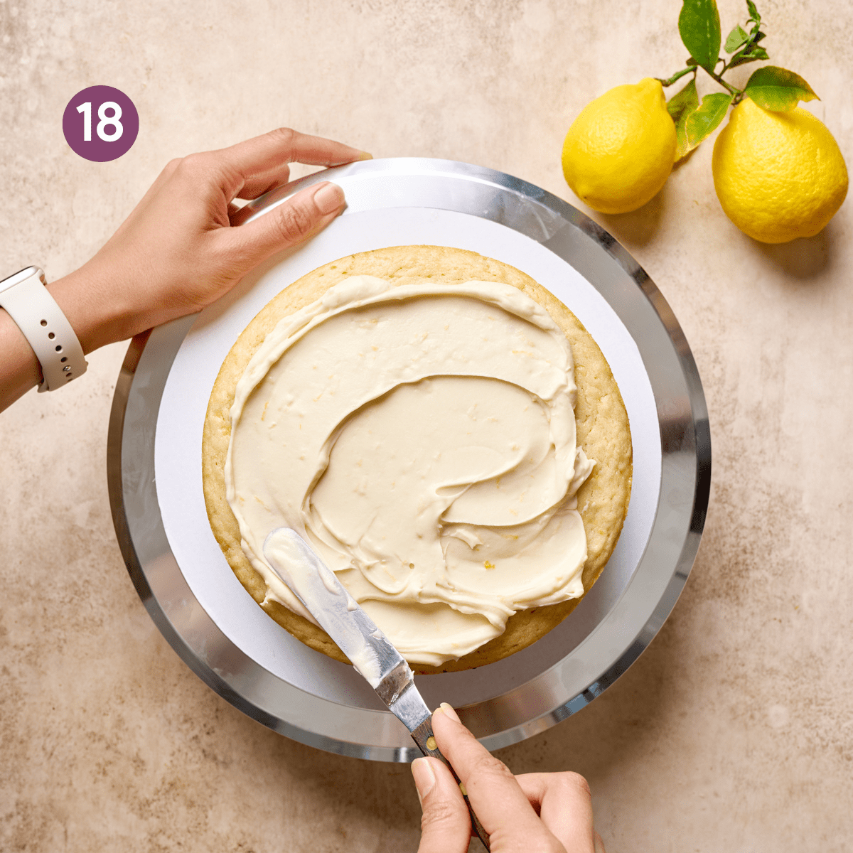 woman's hands using a frosting spatual to frost a vegan lemon cake on a cake stand.