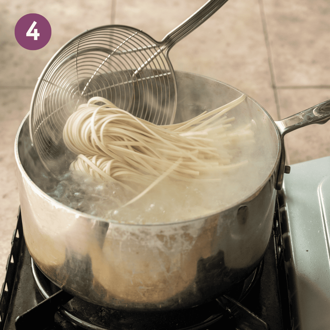 person using a spider tool to drop noodles into boiling water.