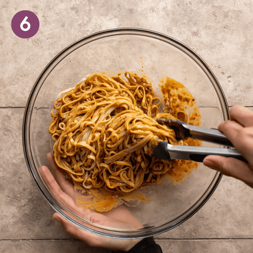 person using tongs to mix noodles and sauce in a bowl.