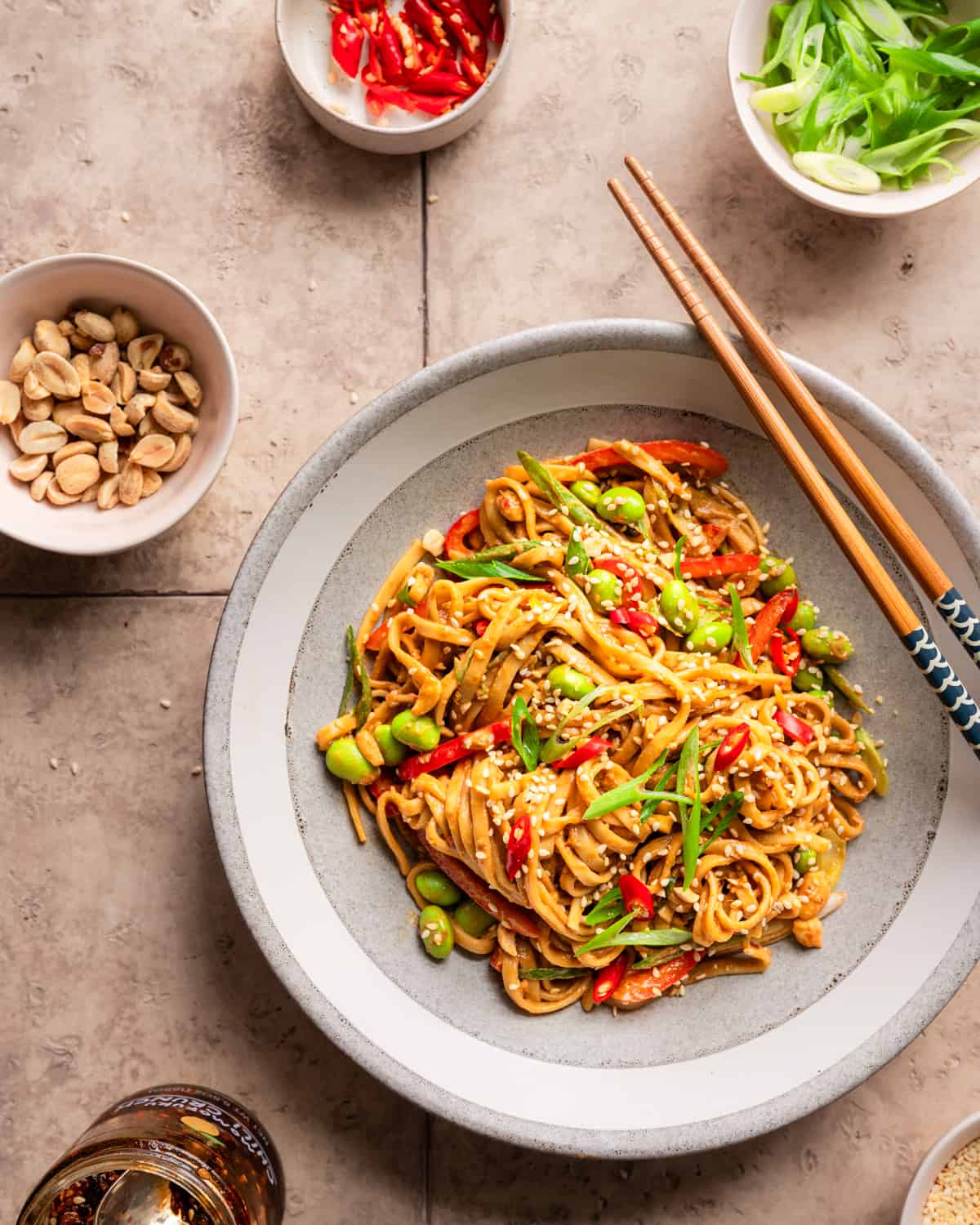sesame noodles in a bowl with various ingredient bowls around it.
