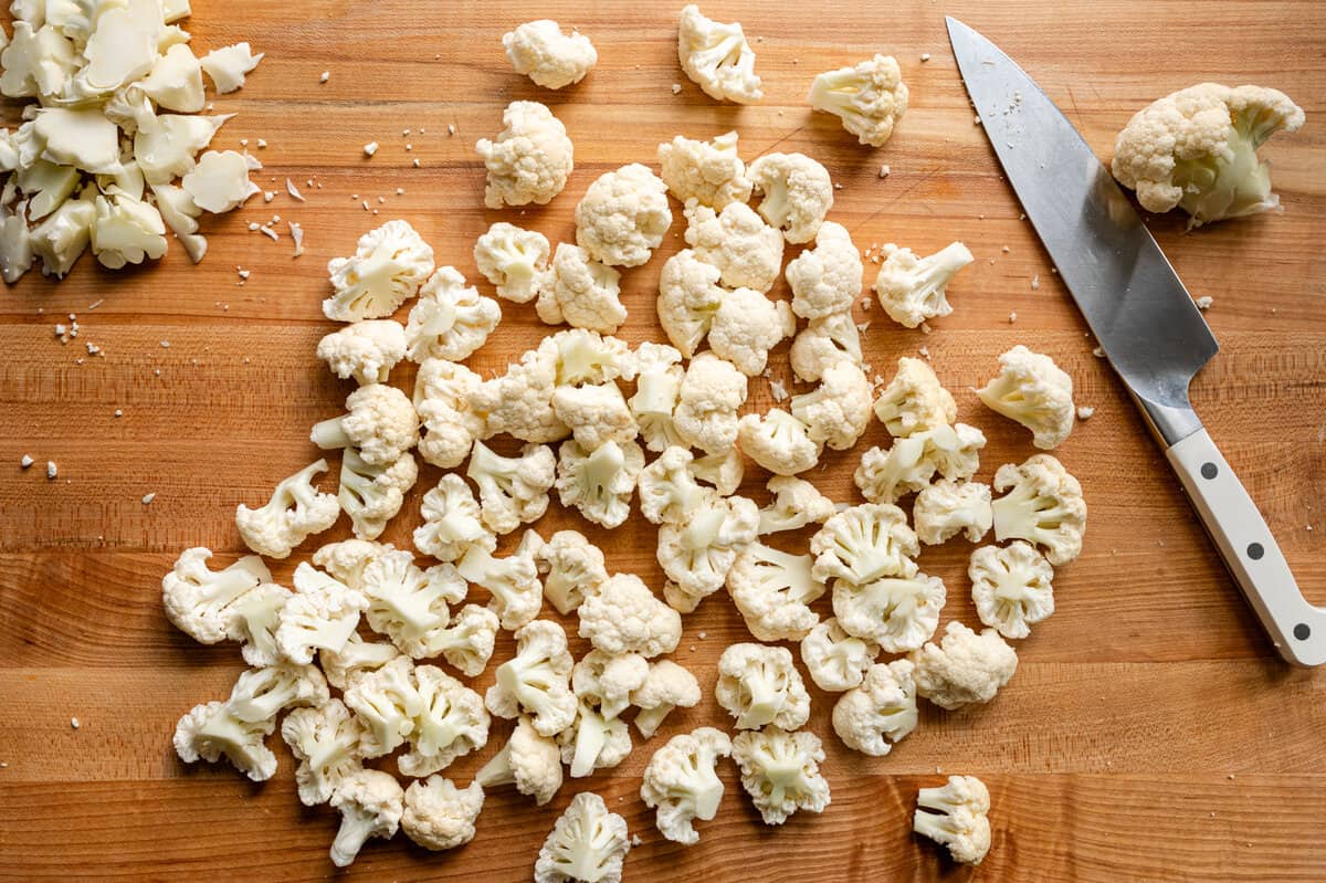 buffalo cauliflower florets and a knife on a wooden cutting board.