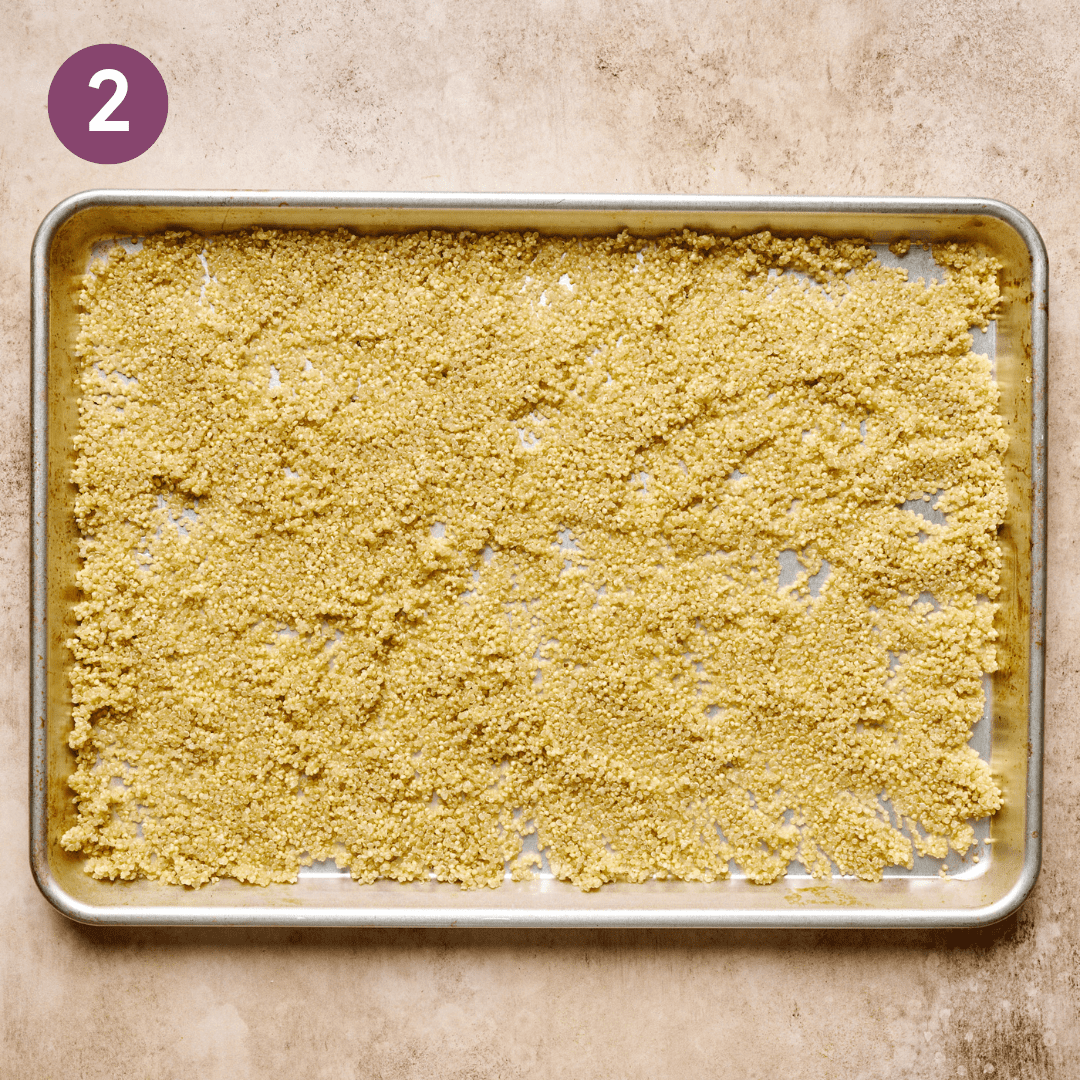 Cooked quinoa spread out on a baking sheet to dry.