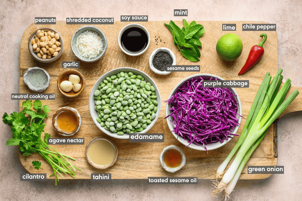 Edamame salad ingredients in various bowls on a wooden cutting board.